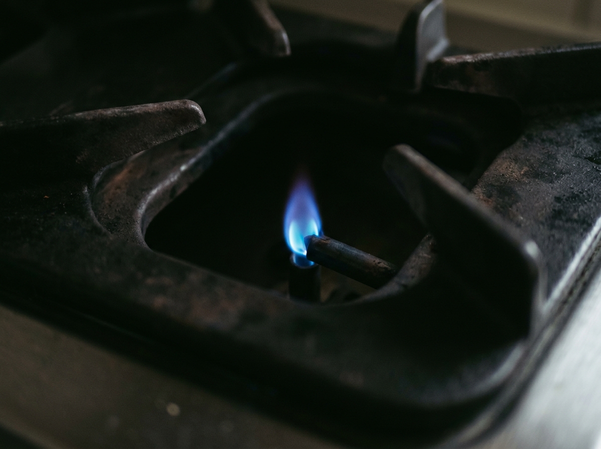 A steady blue pilot flame burning inside a dark metal gas burner housing